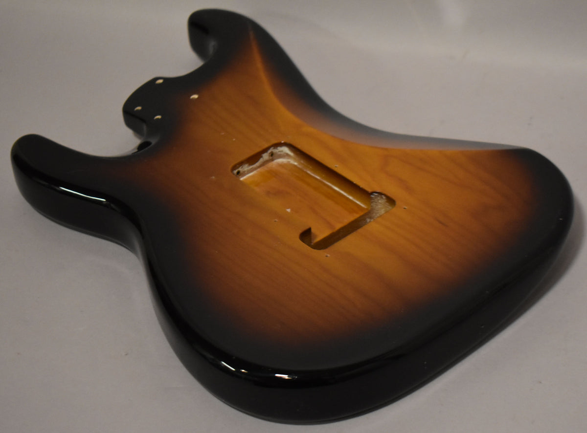 The Stratocaster body, in a glossy 2-tone sunburst, is angled to show the back with a rectangular tremolo cavity and neck pocket.