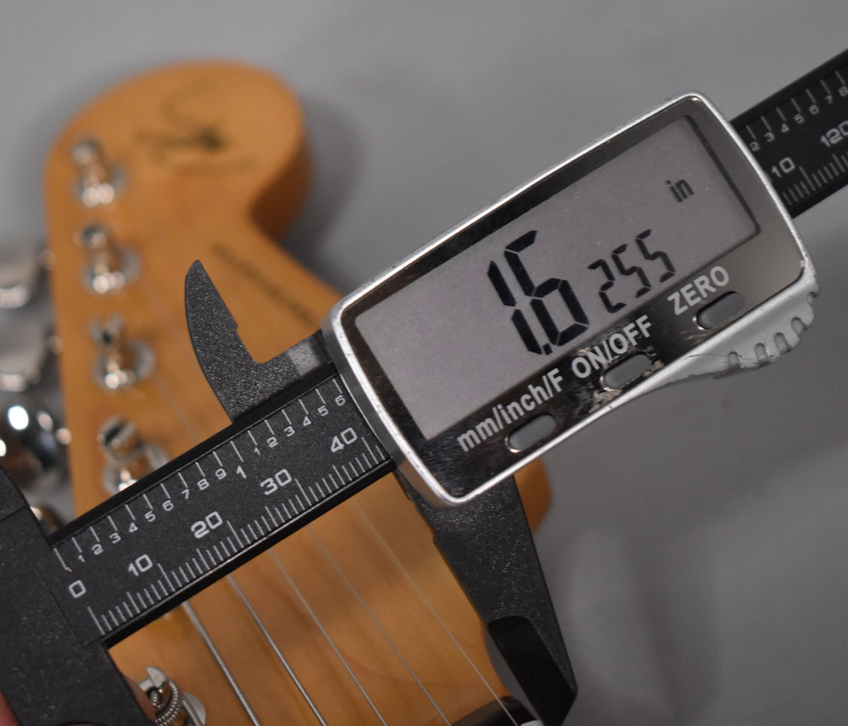 Digital calipers measure a guitar neck, displaying "1.6 255 in".