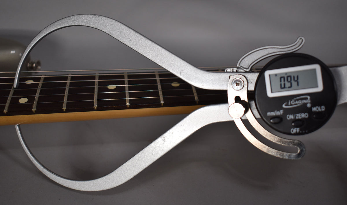 A digital caliper measures the neck thickness at the first fret, showing 0.94 inches, with a dark rosewood fretboard and dot inlays.
