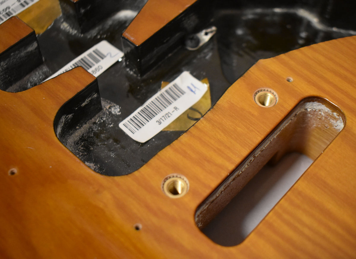 Close-up of the sunburst body's control cavity, showing two brass threaded inserts and a white barcode sticker dated 3/17/21-R.