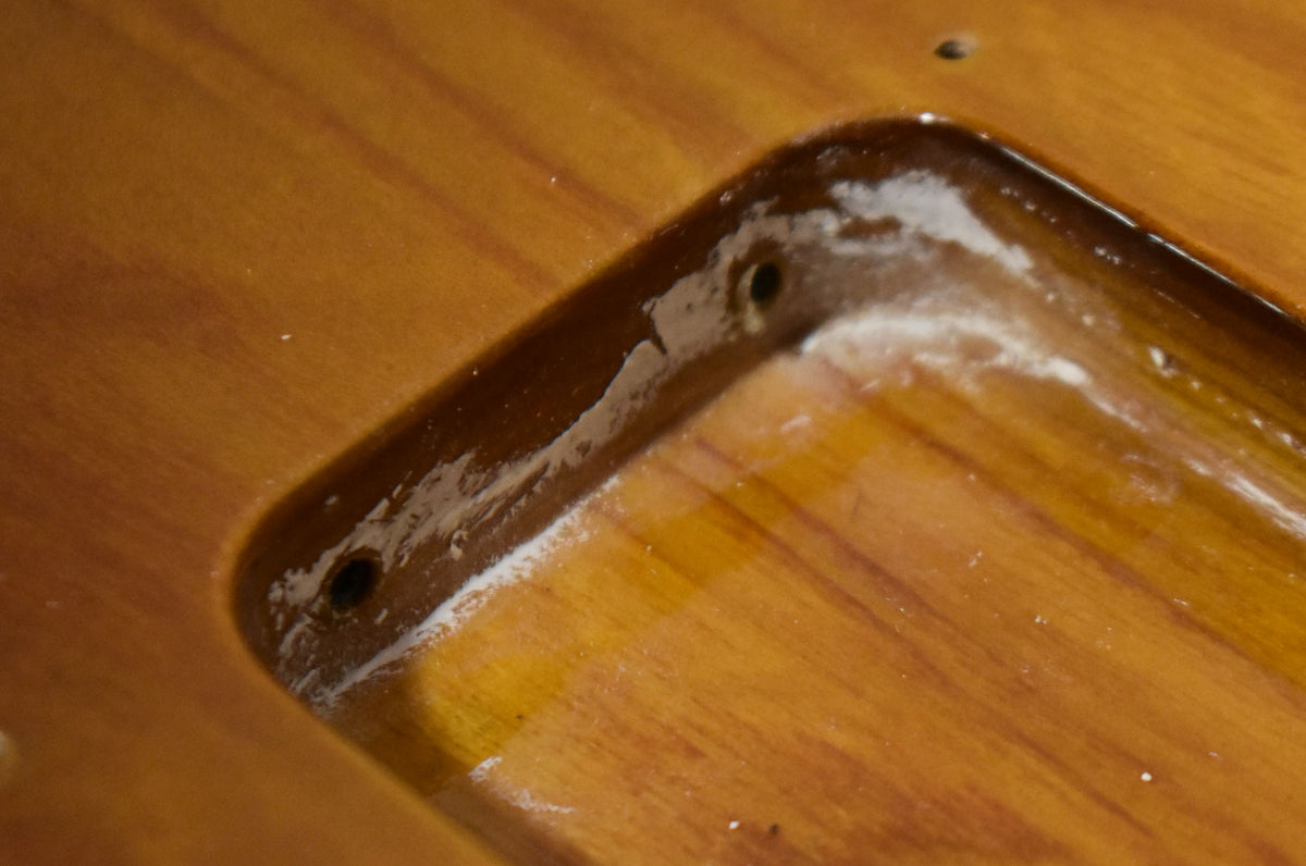 Close-up of the sunburst body's neck pocket, showing two screw holes and white residue along the edges.