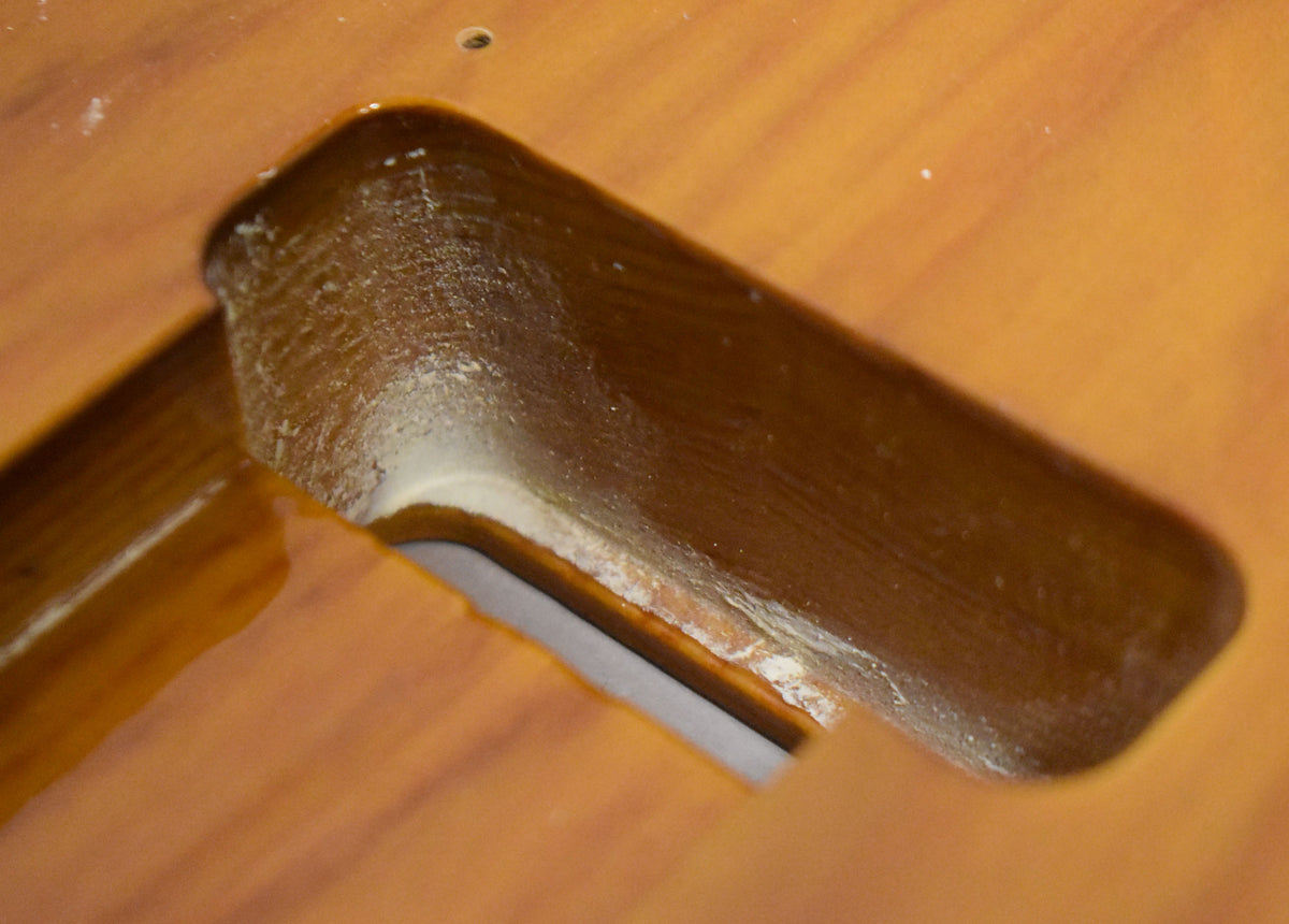 Close-up of the dark brown pickup cavity, showing rough wood and white residue inside, with a small screw hole above.