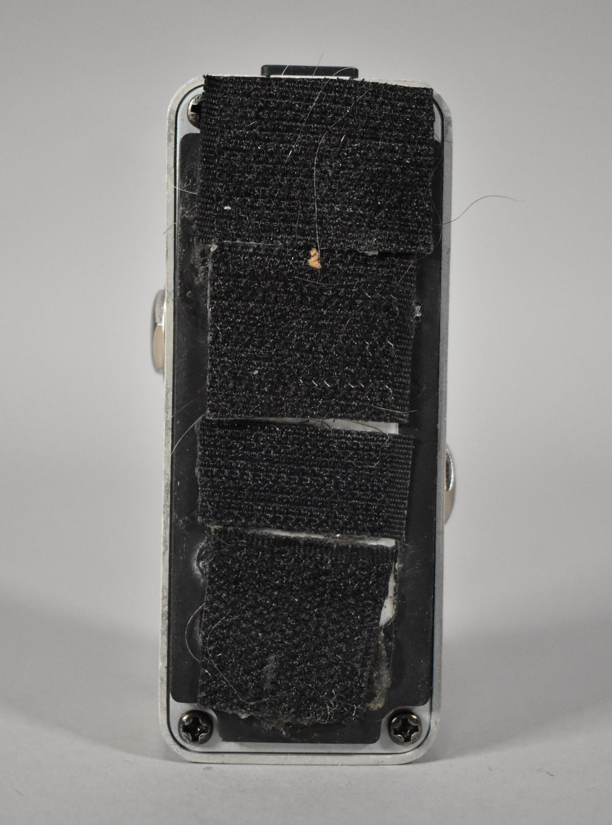 The bottom of the silver pedal is covered in worn black hook-and-loop strips, with visible lint and a small brown speck.