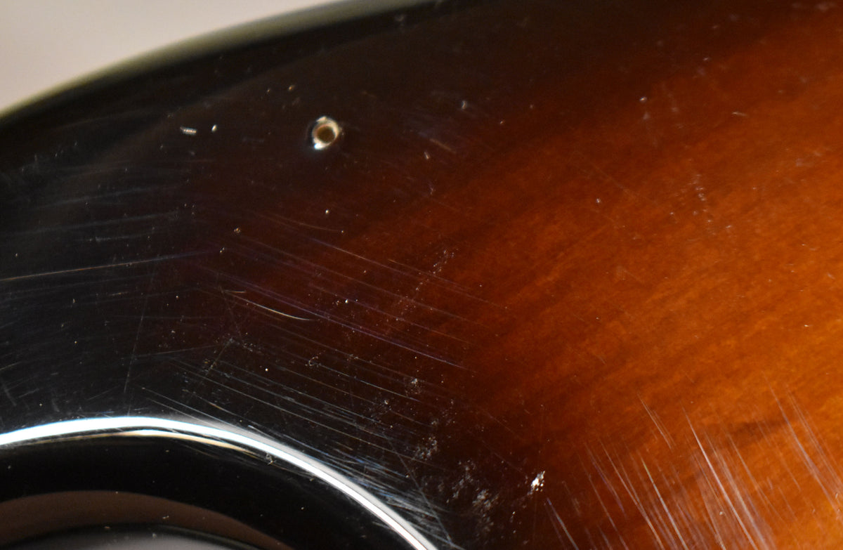 Close-up of the upper horn of a glossy 2-tone sunburst Stratocaster body, showing many scratches and a single screw hole.