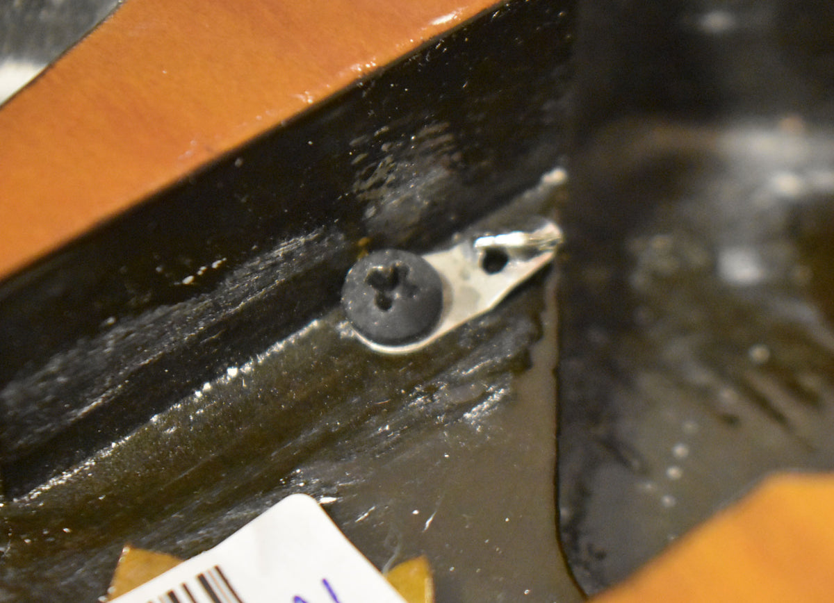 Close-up of a black screw and a silver strap button on the dark brown edge of the guitar body, with a white sticker visible.