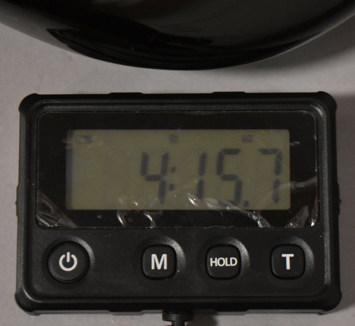 A digital scale displays "4:15.7" with "lb" and "oz" indicators, below a black curved object.