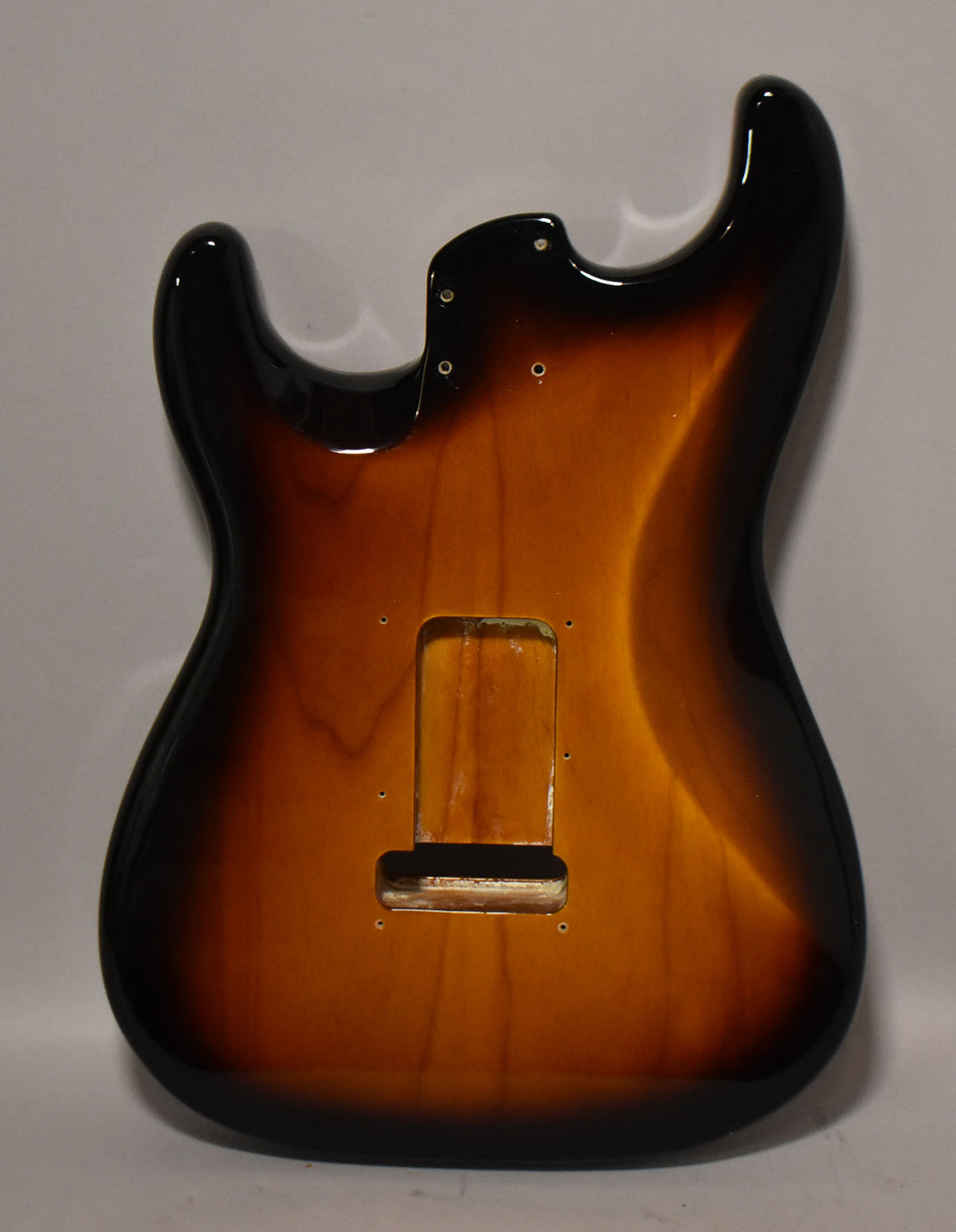 The back of a glossy 2-tone sunburst Stratocaster body, showing the tremolo cavity and neck plate screw holes.