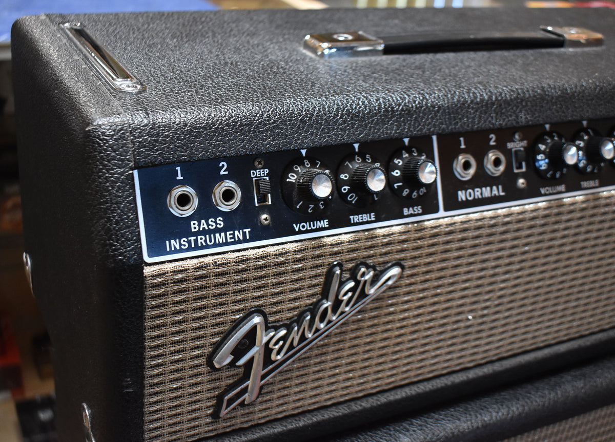 Close-up of the black amp head's textured top and front panel, showing silver controls, a black handle, and a brown grille cloth.