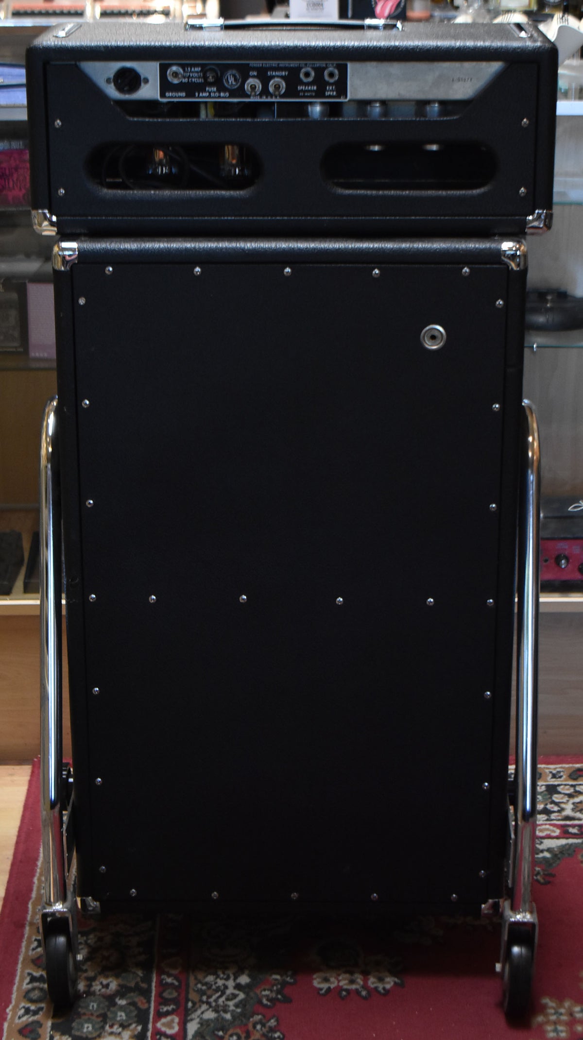 Rear view of the black tolex amp head and cabinet on a chrome trolley, showing the head's silver control panel and exposed tubes.