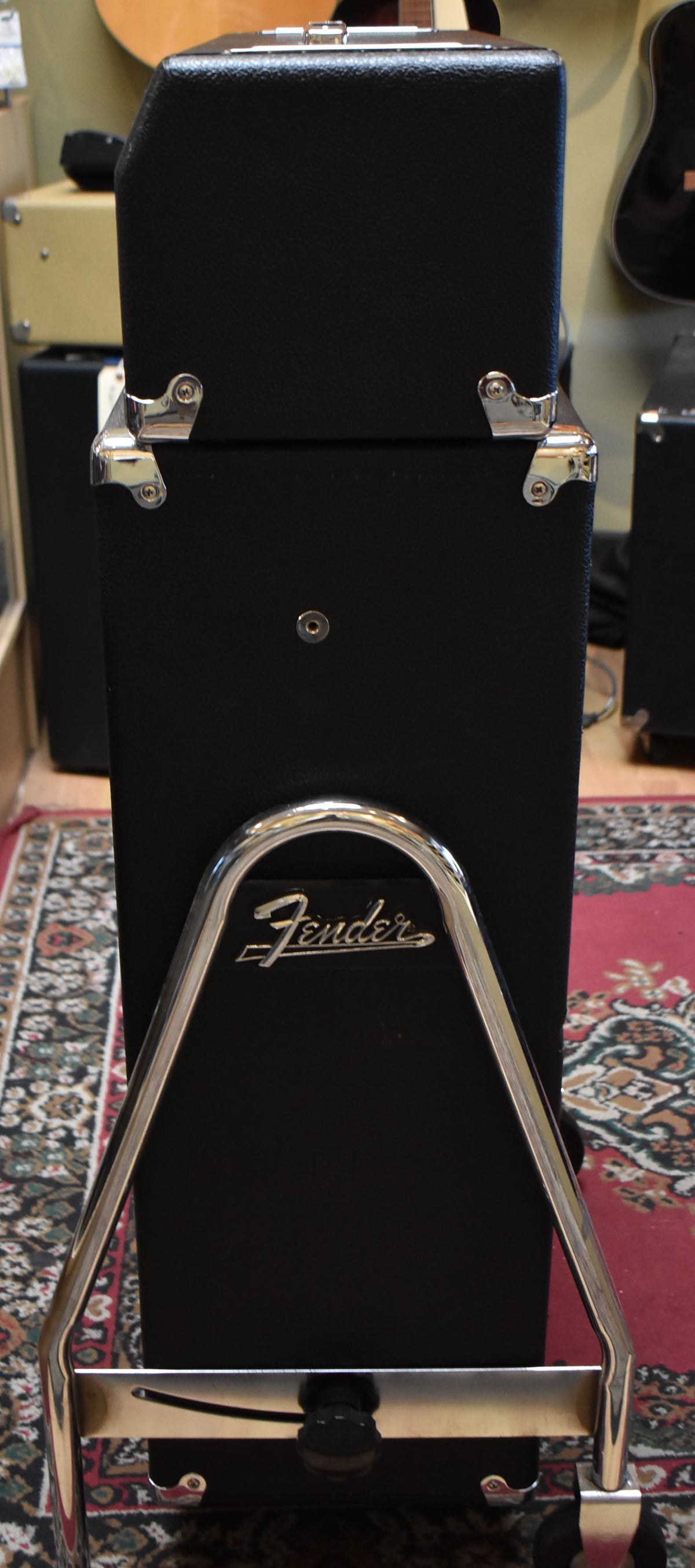 Full-height view of the black amp and cabinet on a chrome trolley, showing the side of the head and the front of the cabinet.