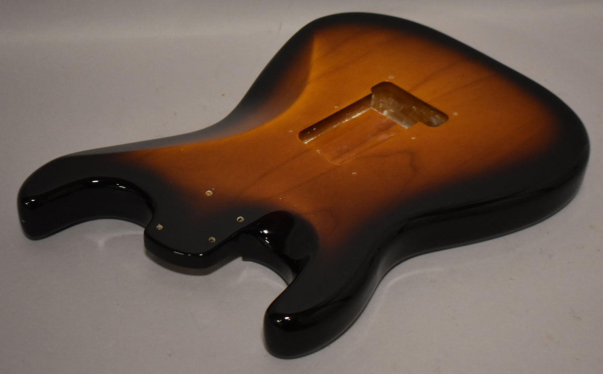 The Stratocaster body, in a glossy 2-tone sunburst finish, is angled to show the back, with a tremolo cavity and screw holes visible.