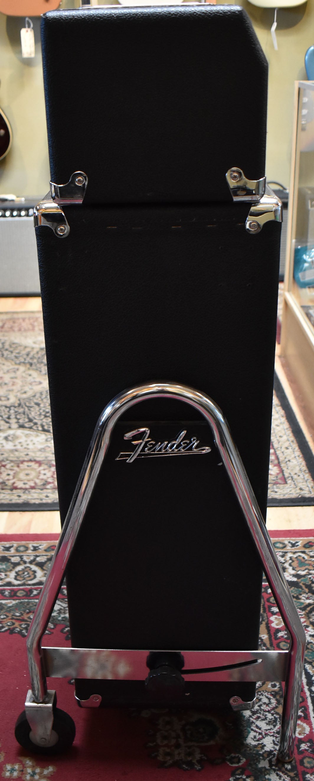 Rear view of the black amp cabinet on a chrome trolley with casters, showing the chrome logo and corner protectors.