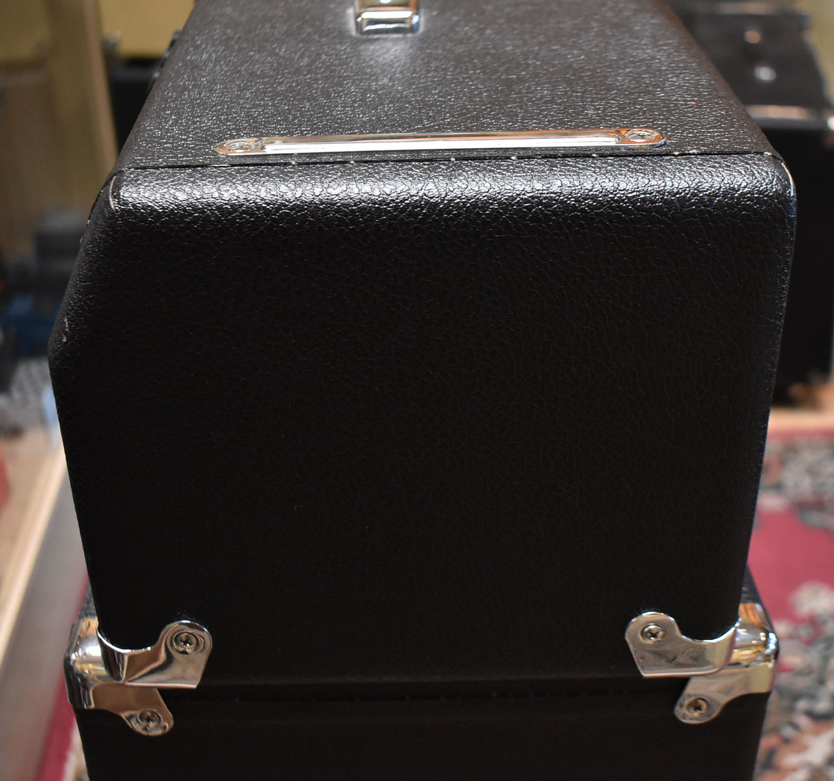 Close-up of the black textured amp head's top and side, showing a silver handle, chrome corner protectors, and minor wear on the top edge.