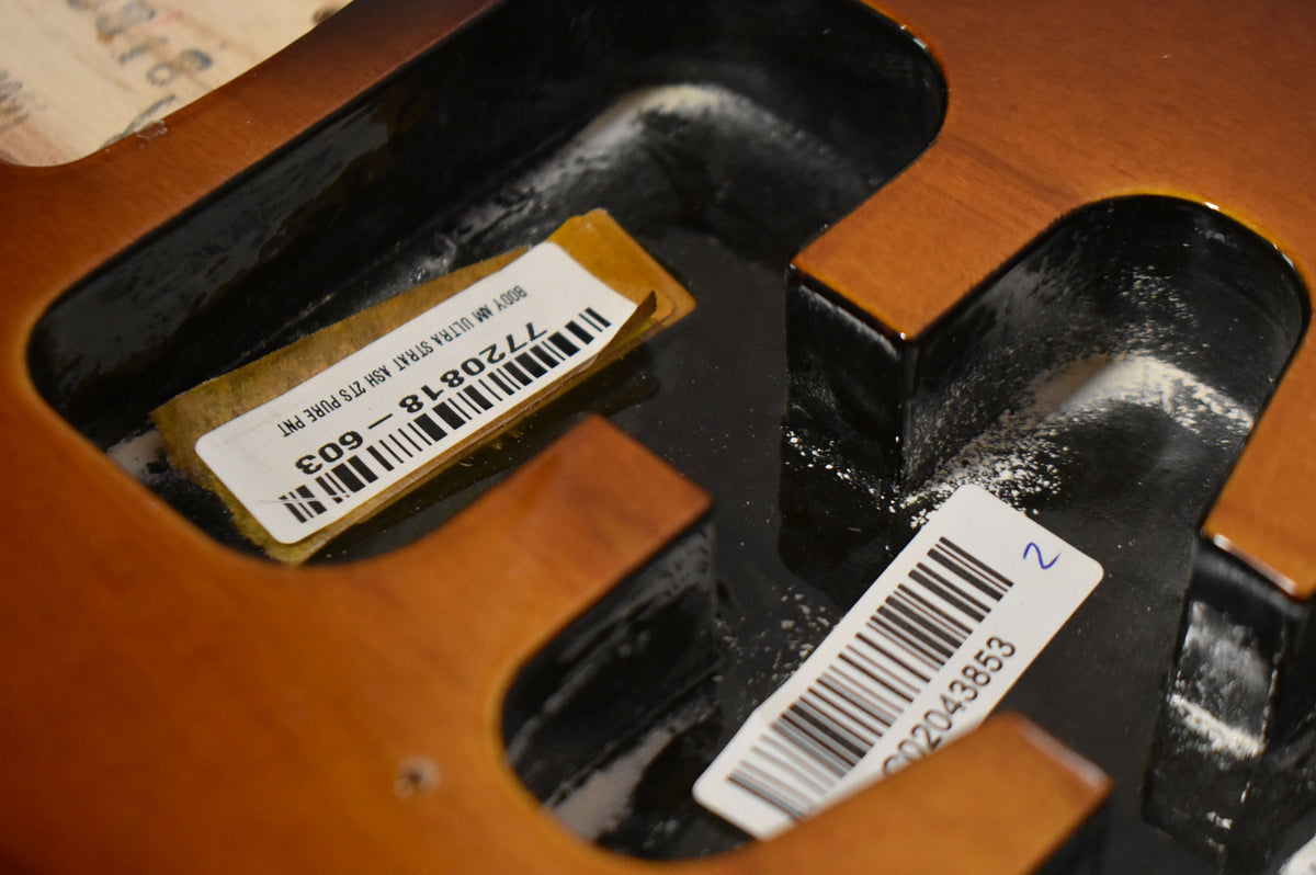 Close-up of the guitar body's dark brown routing cavities, with two white barcode stickers and some white dust visible.