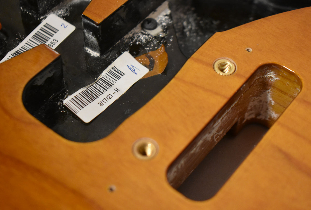 Close-up of the sunburst body's control cavity, showing two threaded brass inserts and a date sticker on the black shielding paint.