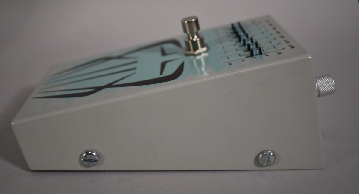 The white pedal is angled right, showing a chrome footswitch, a row of black slider controls, and a silver knurled knob on the right.