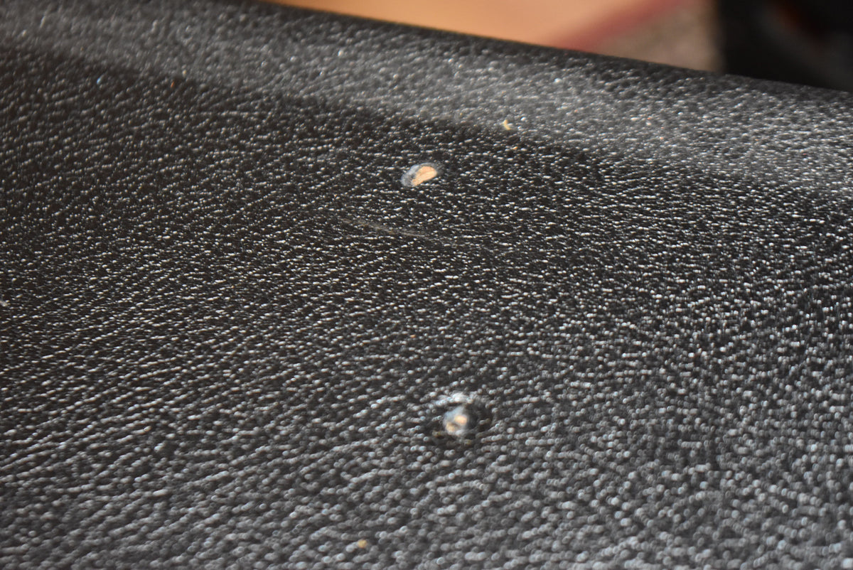 Close-up of the black textured tolex covering, showing two small tears exposing lighter material and a faint scratch.