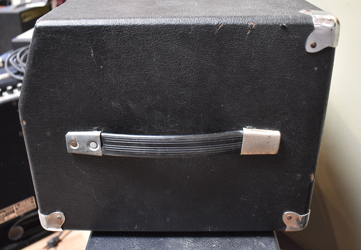 The black tolex-covered amp head is viewed from the side, showing a ribbed black handle with tarnished metal mounts and corner protectors.