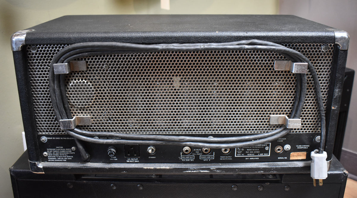 Rear view of the black amplifier head, showing a perforated metal grille, various inputs/outputs, and a power cable.