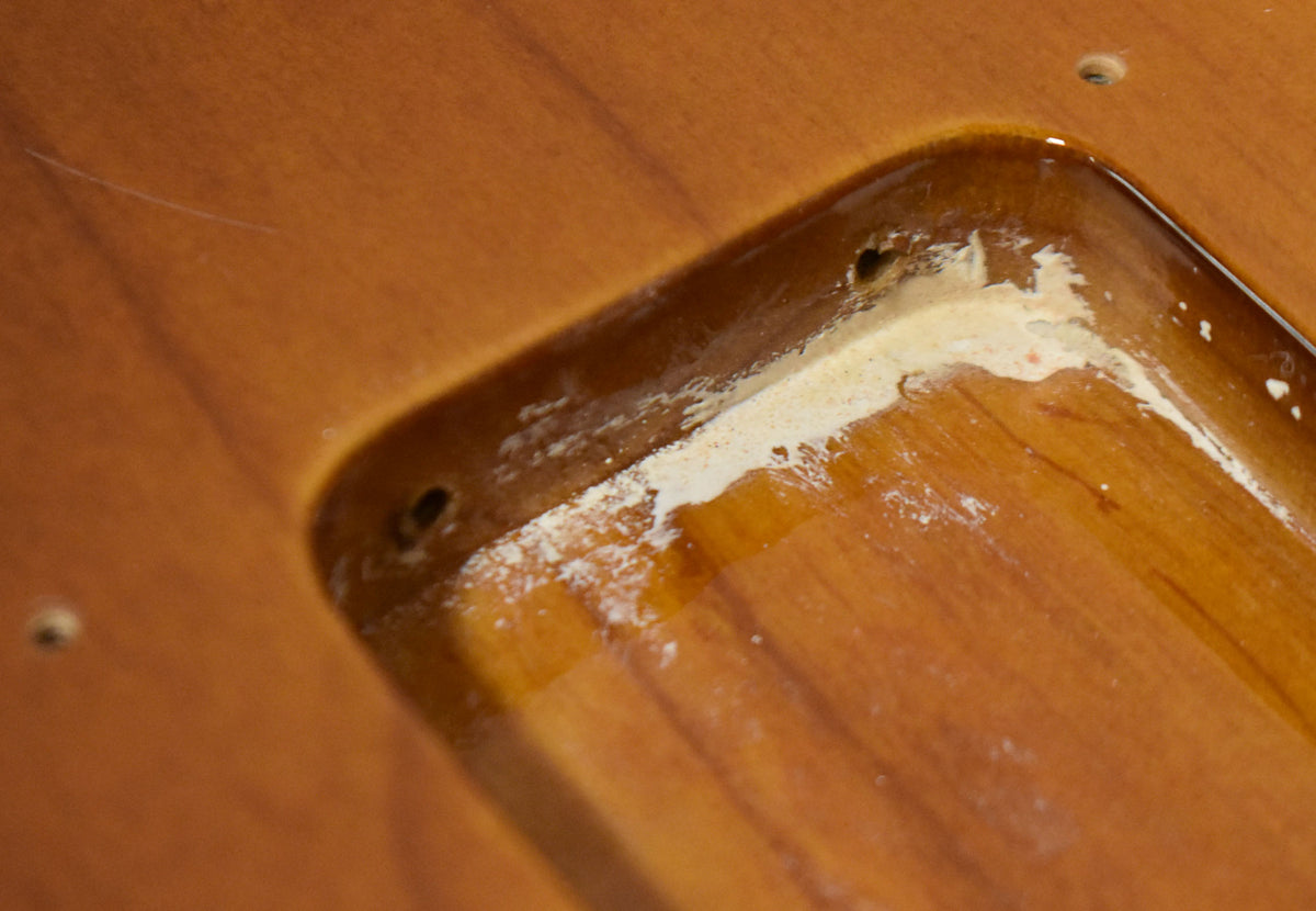 Close-up of the tremolo cavity, showing rough wood and white residue around the screw holes, with a light scratch above.