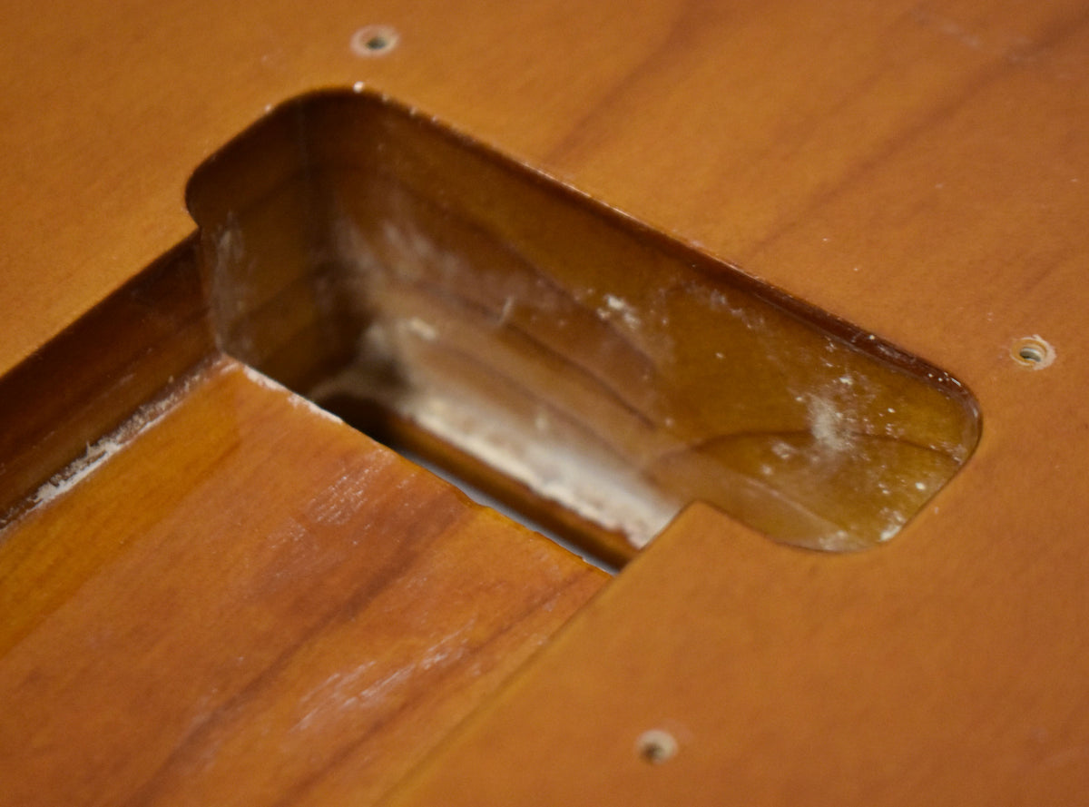Close-up of the sunburst body's tremolo cavity, showing white dust inside and around the edges of the routed opening.