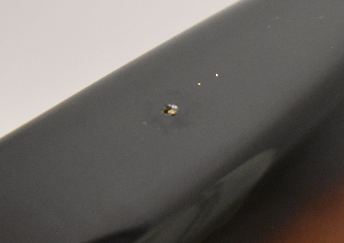 Close-up of a small chip and two tiny white specks on the dark upper edge of the sunburst guitar body.