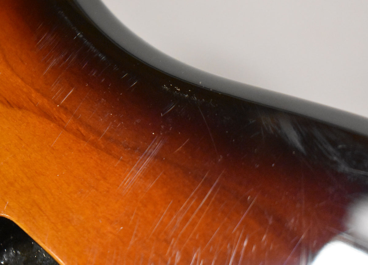 Close-up of the upper horn of a 2-tone sunburst body, showing many light scratches and a few small chips along the dark edge.