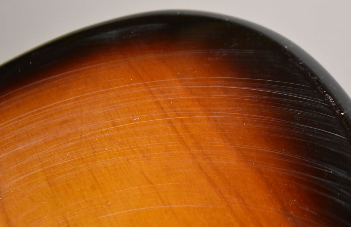 Close-up of the upper bout of a 2-tone sunburst body, showing many fine scratches across the glossy finish.