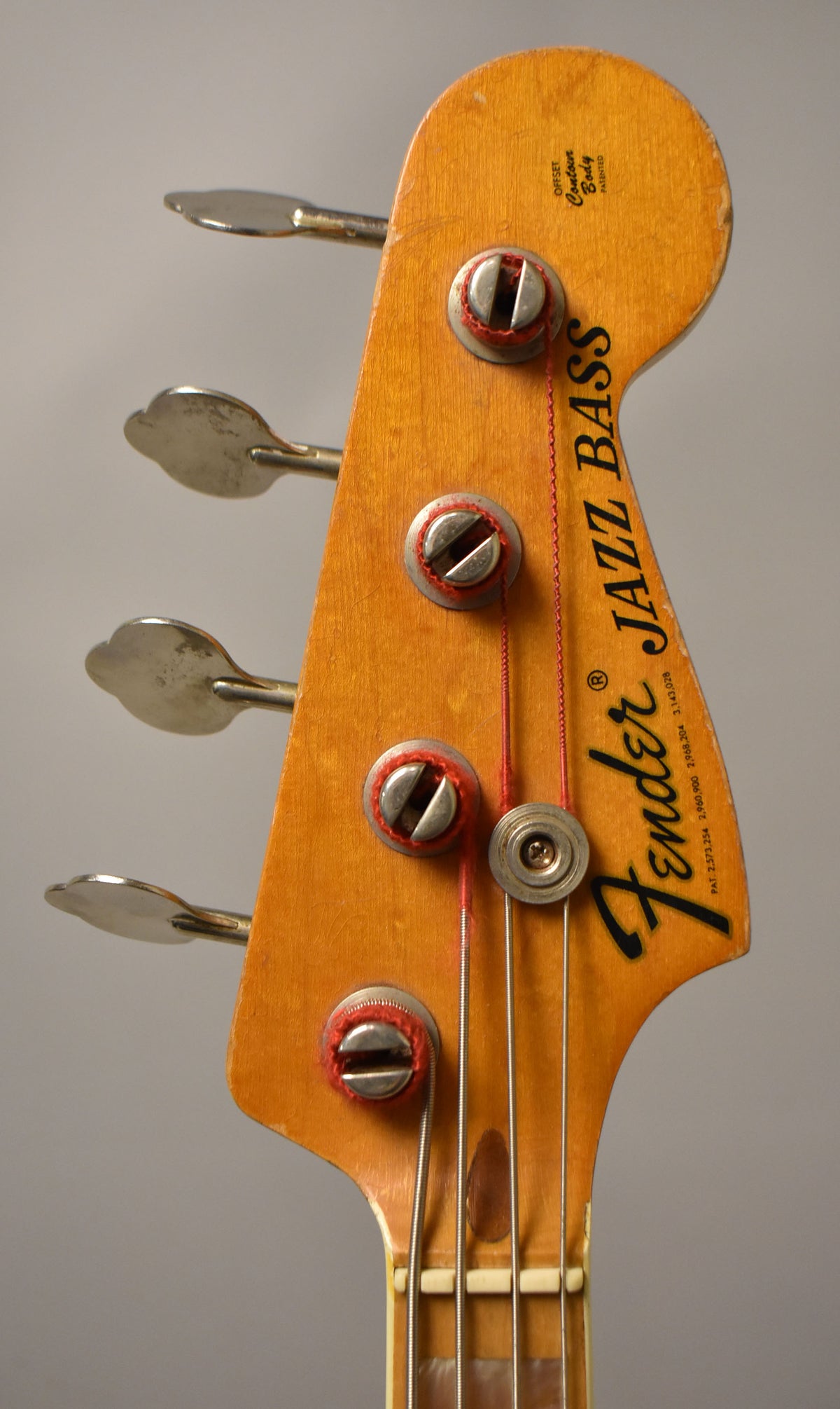 Close-up of the bass headstock, showing the natural wood finish, four silver tuning pegs, and a string tree.