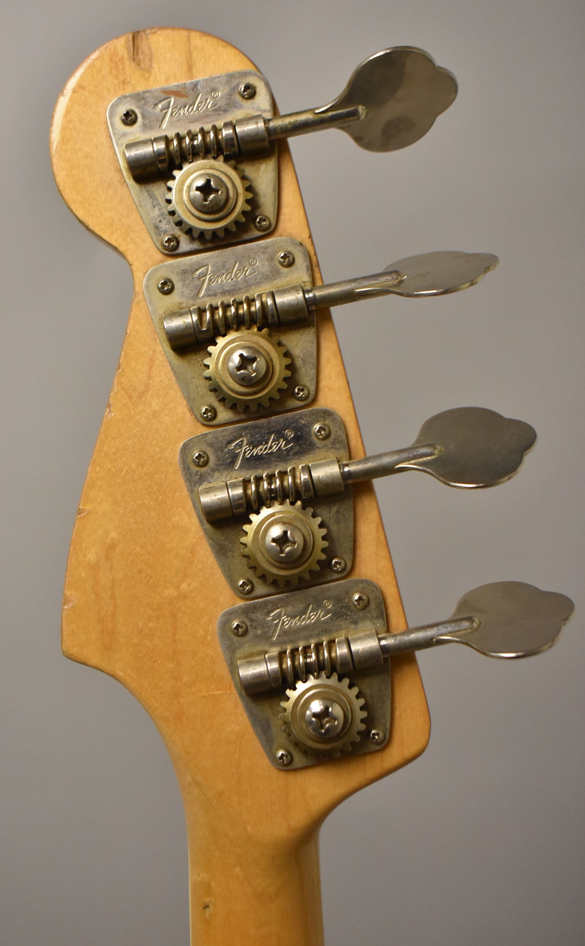 Close-up of the bass headstock's rear, showing four aged chrome tuners with visible wear and a light natural wood finish.