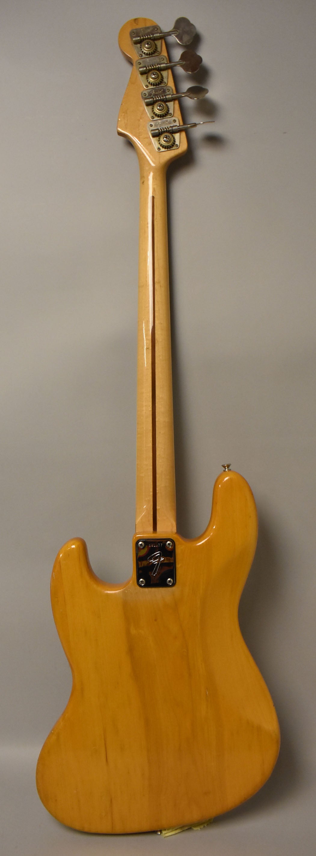 Full rear view of a natural finish bass, showing the maple neck, chrome tuners, and neck plate with light wear.