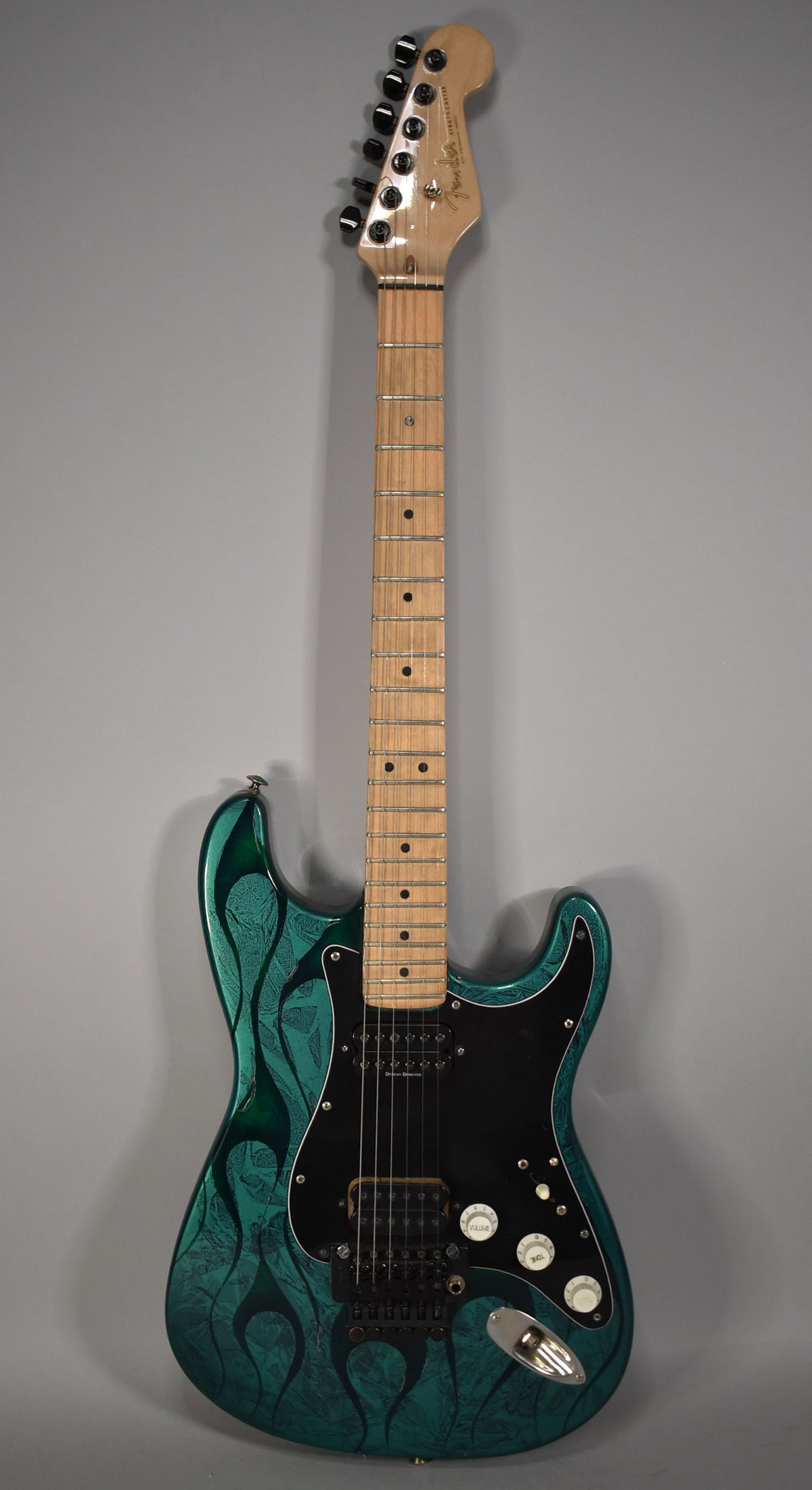 Full front view of a Stratocaster with a green flame finish, black pickguard, two humbuckers, and a Floyd Rose tremolo system.