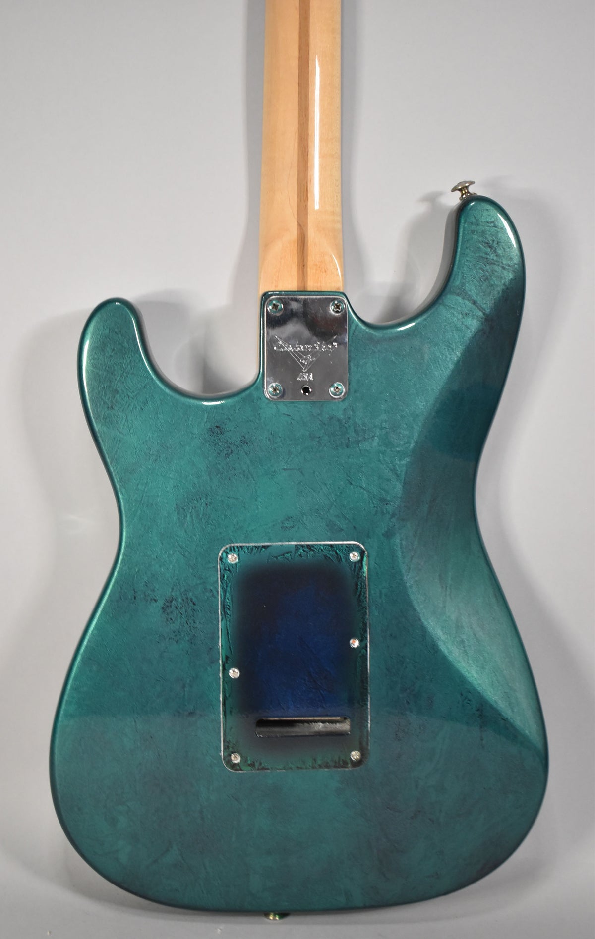 The guitar's back, showing a green flame finish with dark blue undertones, a maple neck, and a chrome neck plate and tremolo cover.