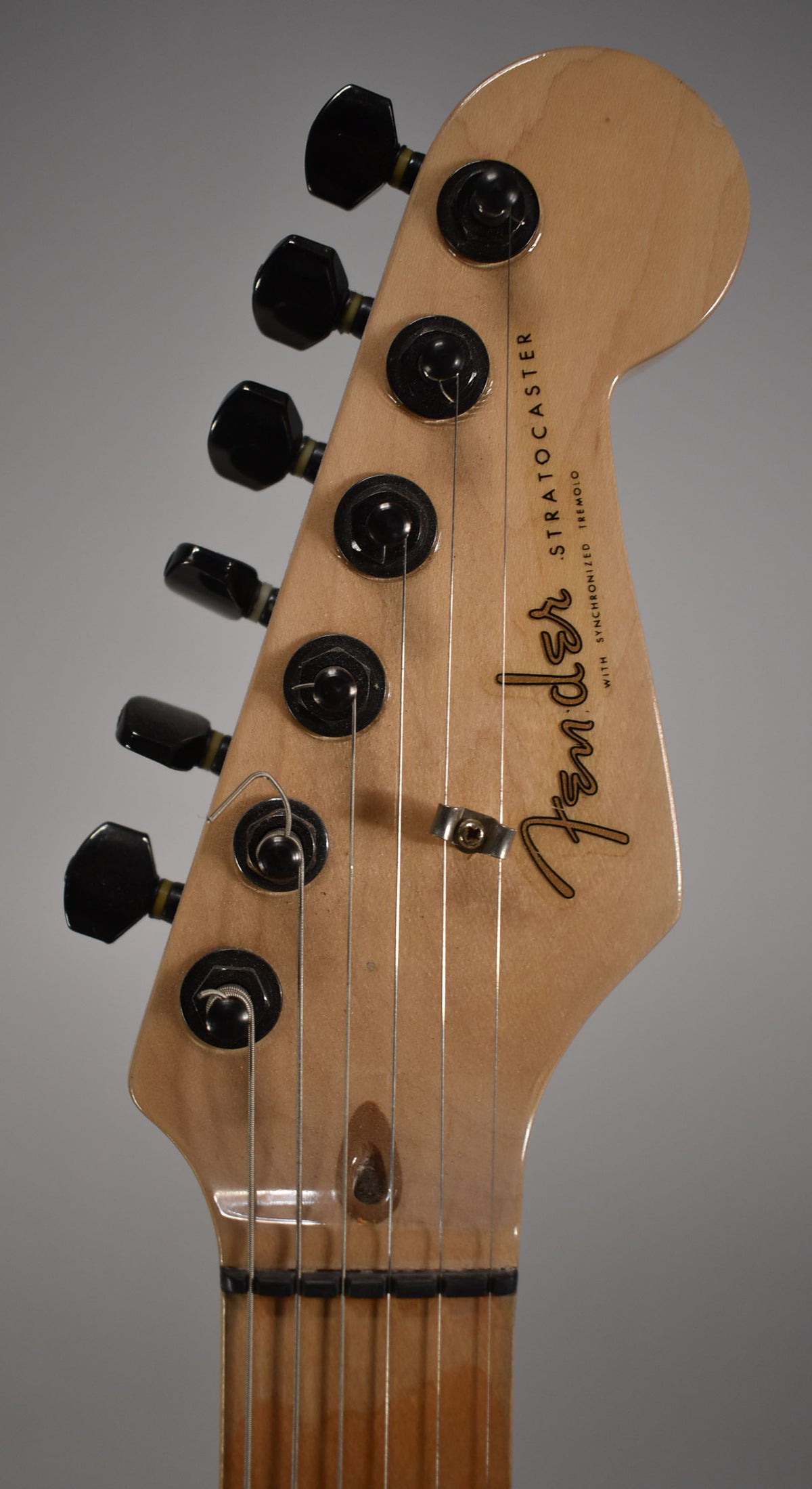Close-up of the light wood headstock with black tuners, showing the string tree and some light wear on the finish.