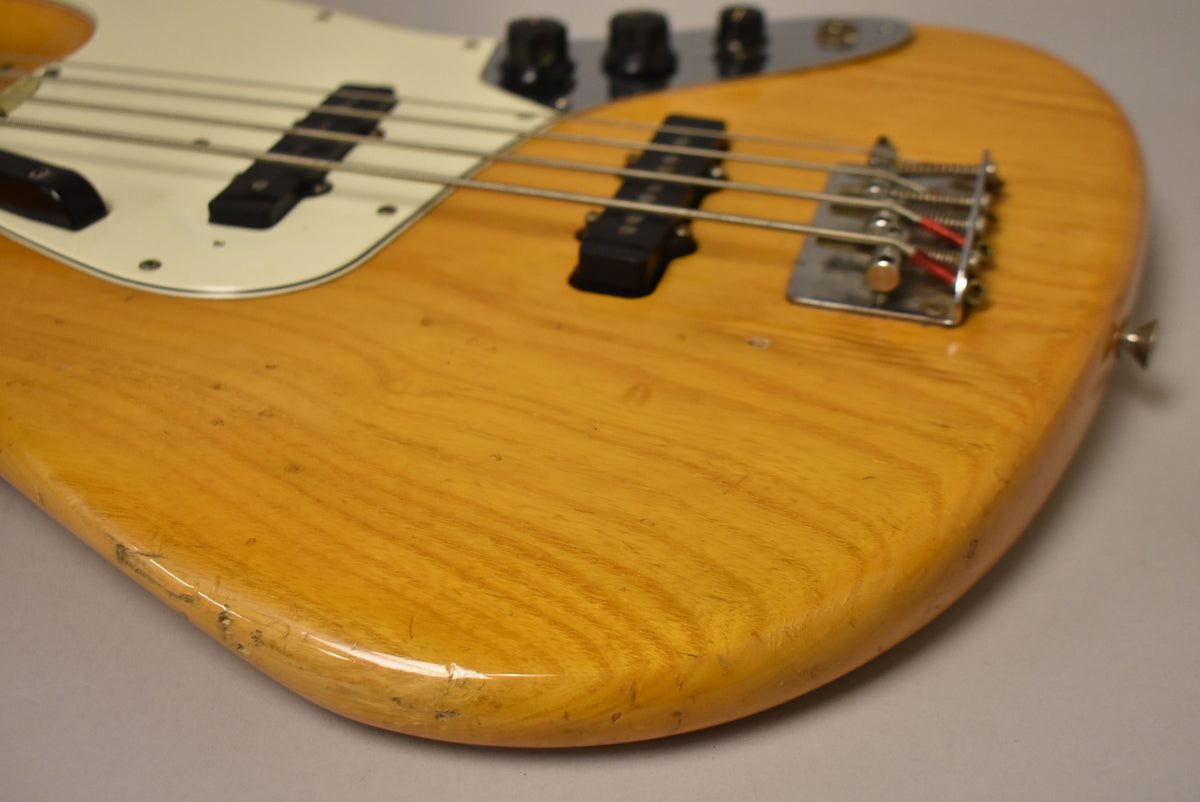 Close-up of the bass body, showing the natural wood grain, white pickguard, bridge, and control knobs, with visible wear and checking.