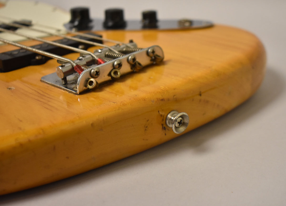Close-up of the natural finish bass body, showing the chrome bridge, output jack, and visible wear and scratches.