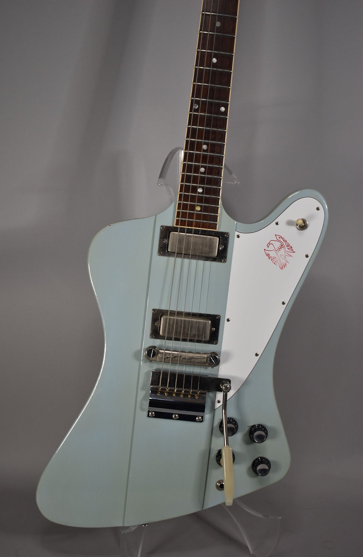 Light blue electric guitar, angled from above, showing the body, three pickups, white pickguard with red bird, and tremolo arm.