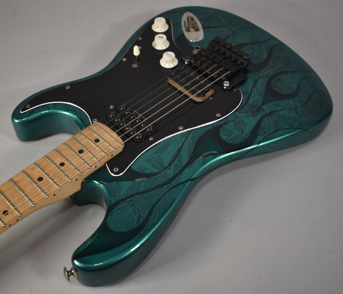 The green flame Stratocaster is angled right, showing the black pickguard, two humbuckers, three white knobs, and maple fretboard.
