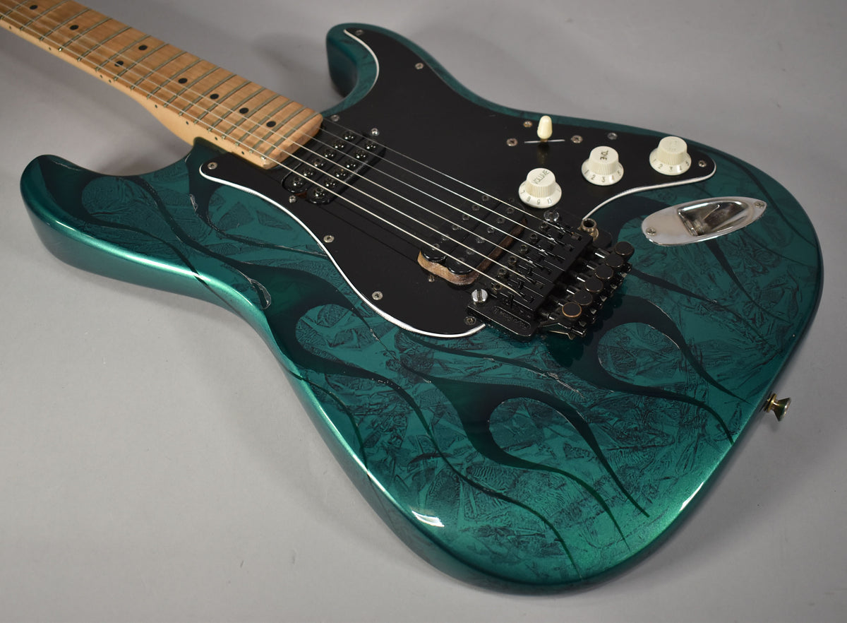 Close-up of the Stratocaster's body and neck, showing the green flame finish with dark green patterns, black pickguard, and black Floyd Rose bridge.