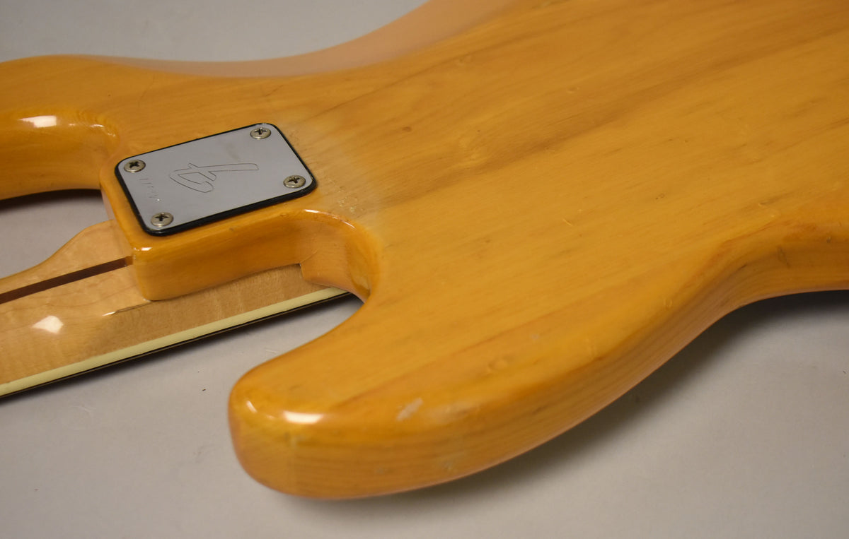Close-up of the natural finish bass body and neck joint, showing the chrome neck plate and light wear on the body.