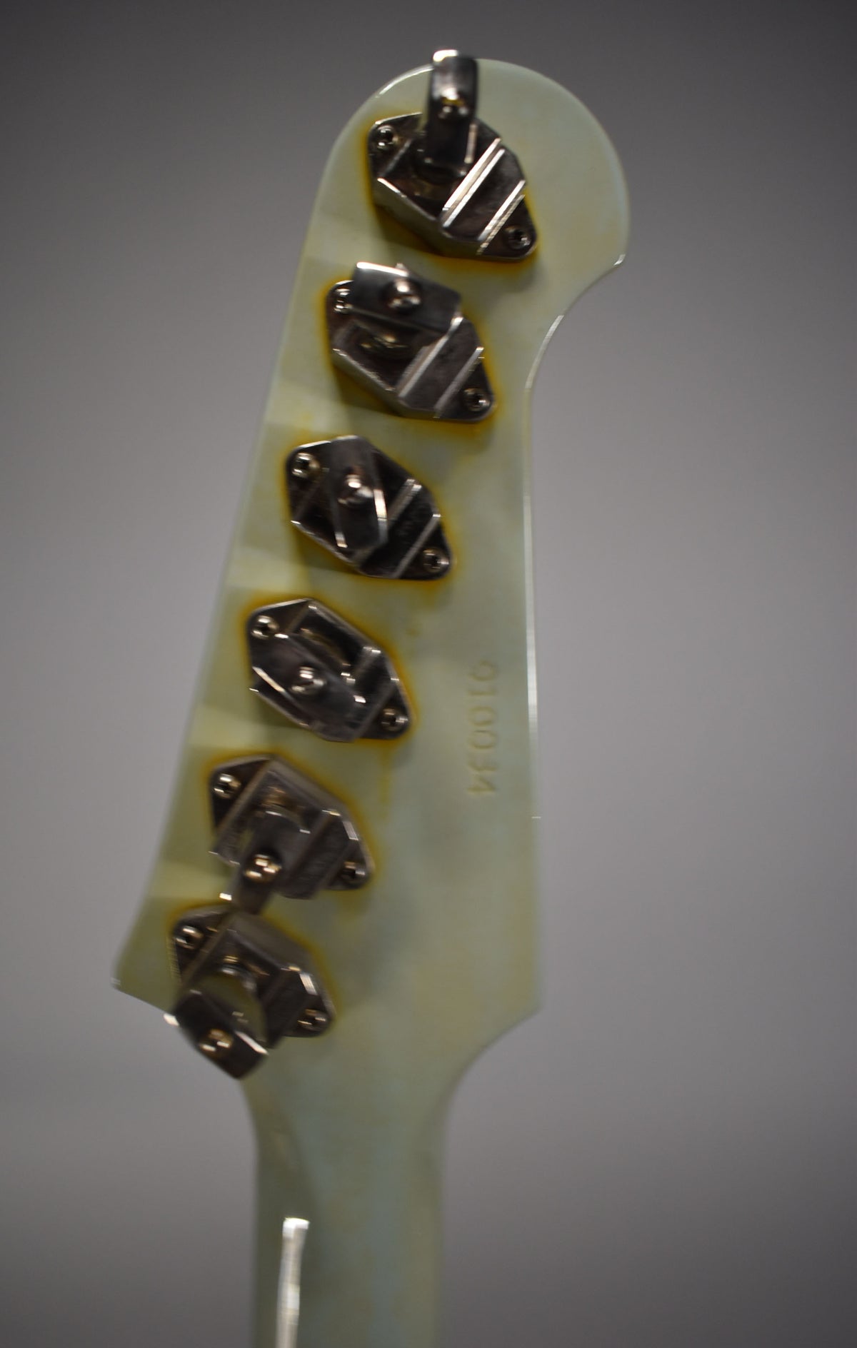 The guitar's headstock, viewed from the back, shows six chrome banjo-style tuners on a cream-colored surface with yellowed edges.