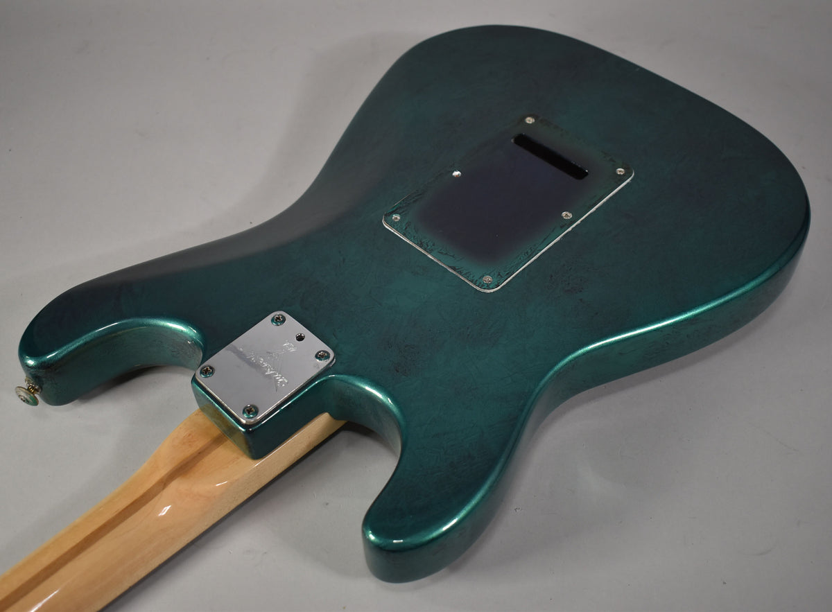 The back of the green flame finish Stratocaster body, showing the neck plate, a dark tremolo cover, and light wear.