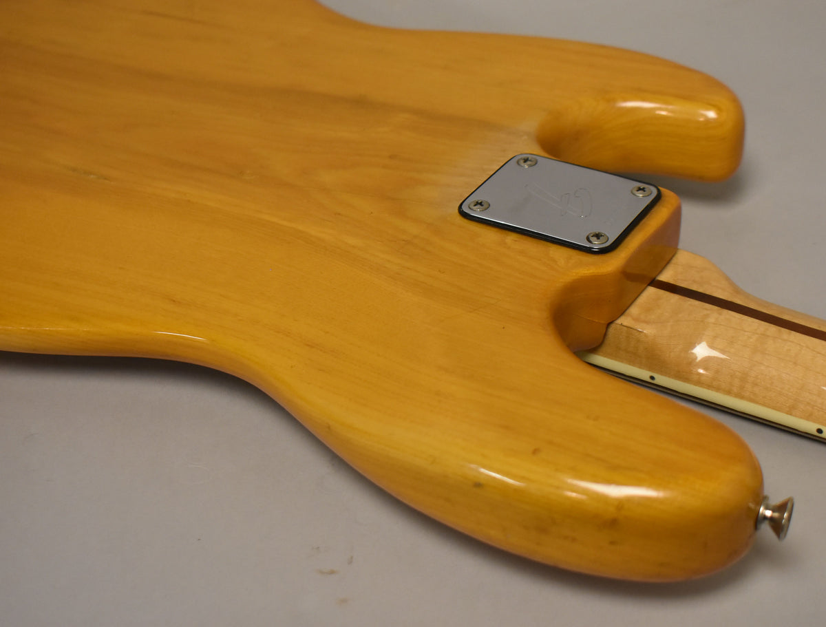 Close-up of the bass's natural finish body and neck joint, showing the chrome neck plate, strap button, and minor wear.