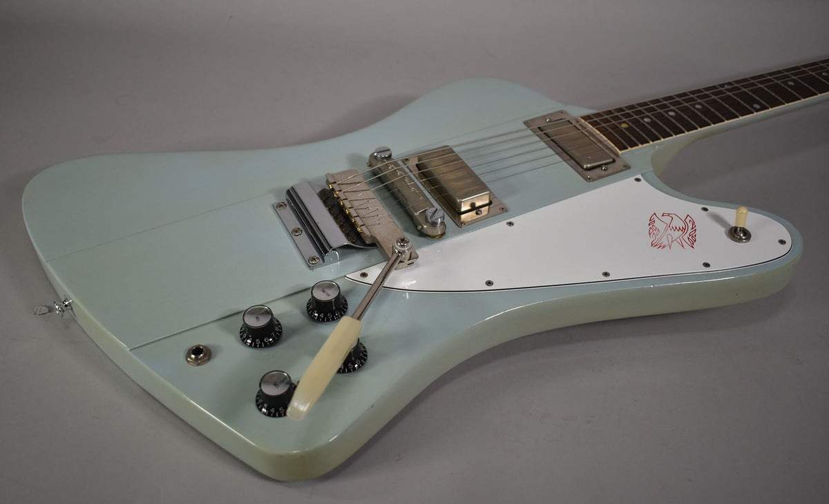 Light blue electric guitar, angled from above, showing the body, white pickguard with red bird logo, and chrome hardware.