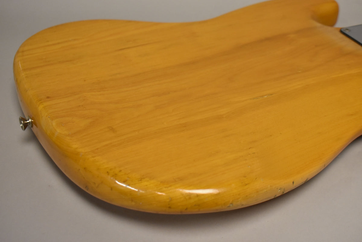 Close-up of the bass's natural finish body back, showing wood grain, a strap button, and light wear along the lower edge.