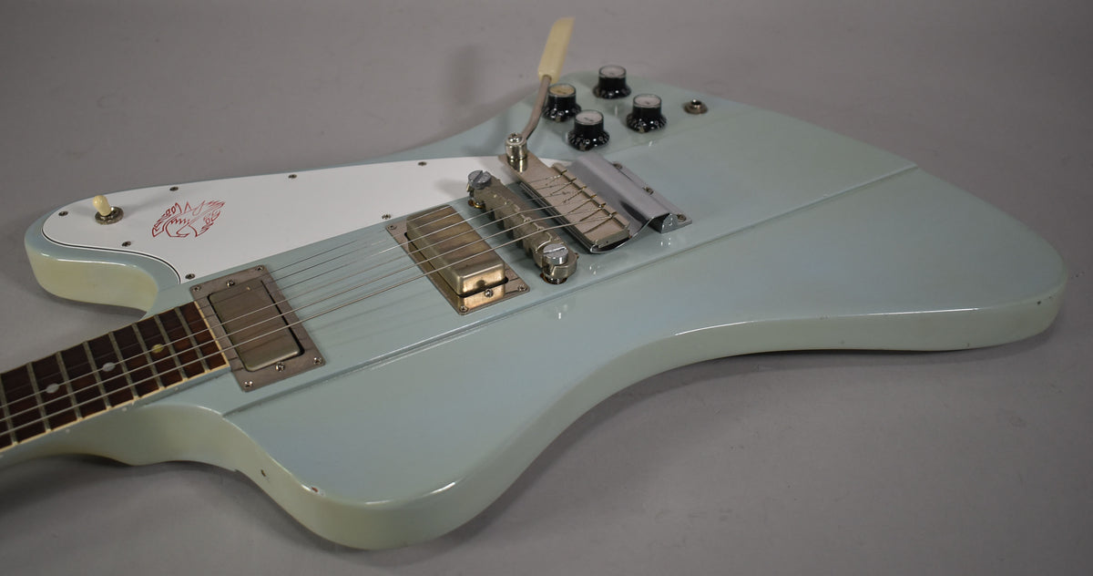 The Frost Blue guitar body is angled from the neck, showing a white pickguard with red bird graphic, two pickups, and a vibrato.