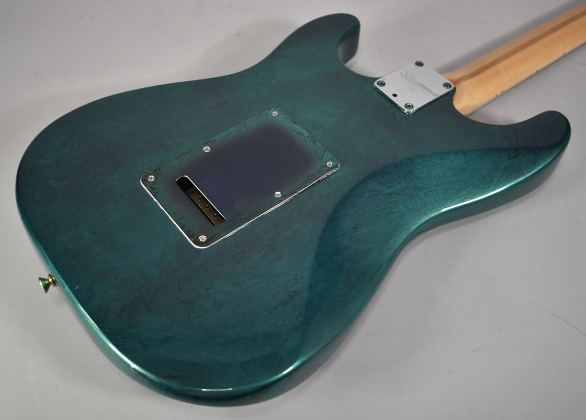 The back of a green flame finish Stratocaster body, showing a dark blue tremolo cavity cover and a chrome neck plate.