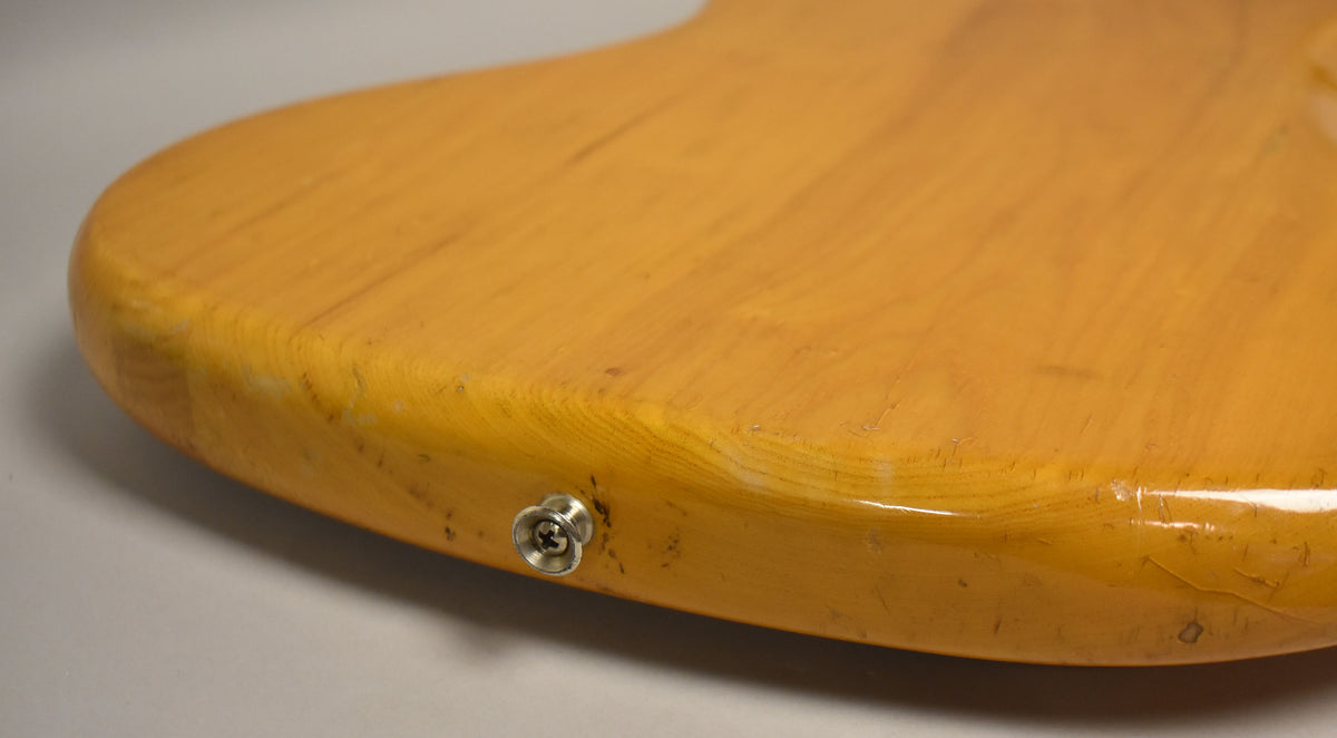 Close-up of the bass's lower bout, showing the natural finish, output jack, and visible wear and checking on the body.