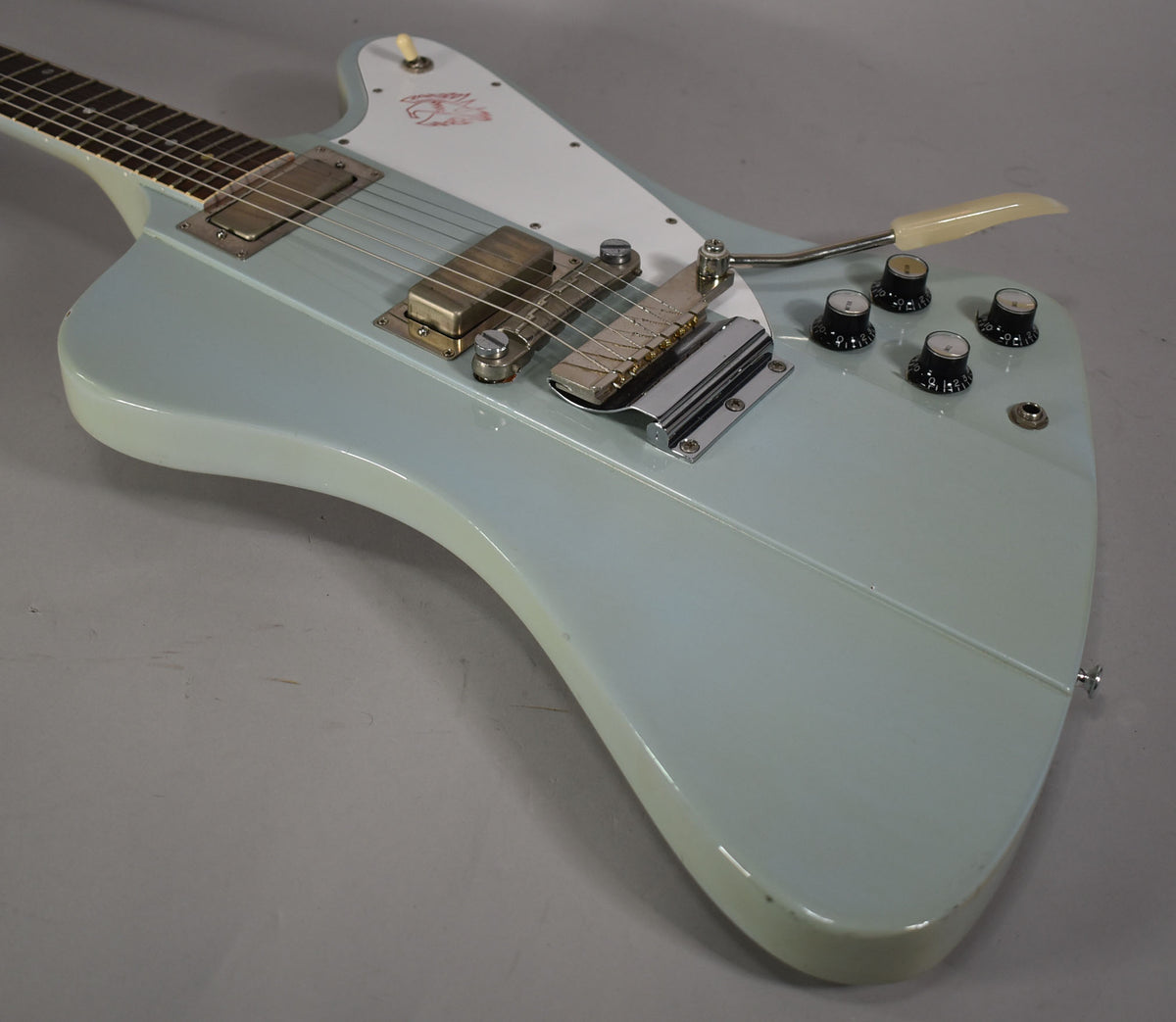 Close-up of the light blue guitar body, showing two gold humbuckers, a white pickguard, four black control knobs, and a tremolo arm.