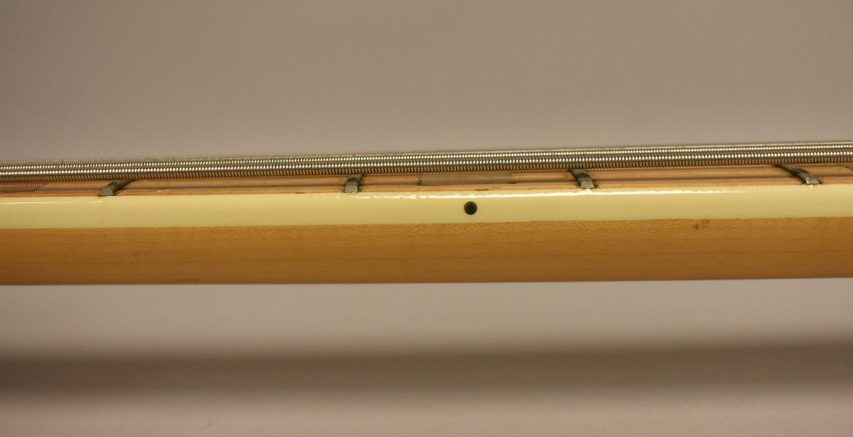 Close-up of the bass neck from the side, showing the light wood, cream binding, frets, and a black dot marker.